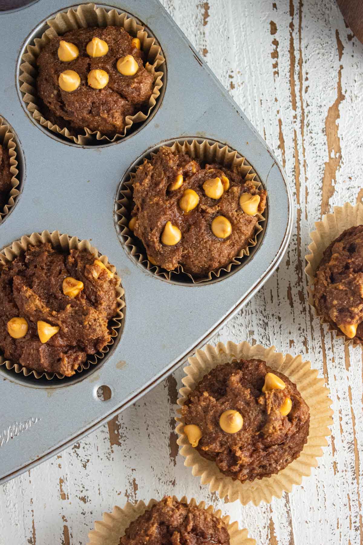 A close-up of pumpkin butterscotch muffins. Half the muffins in a muffin tin and half on a wooden table.