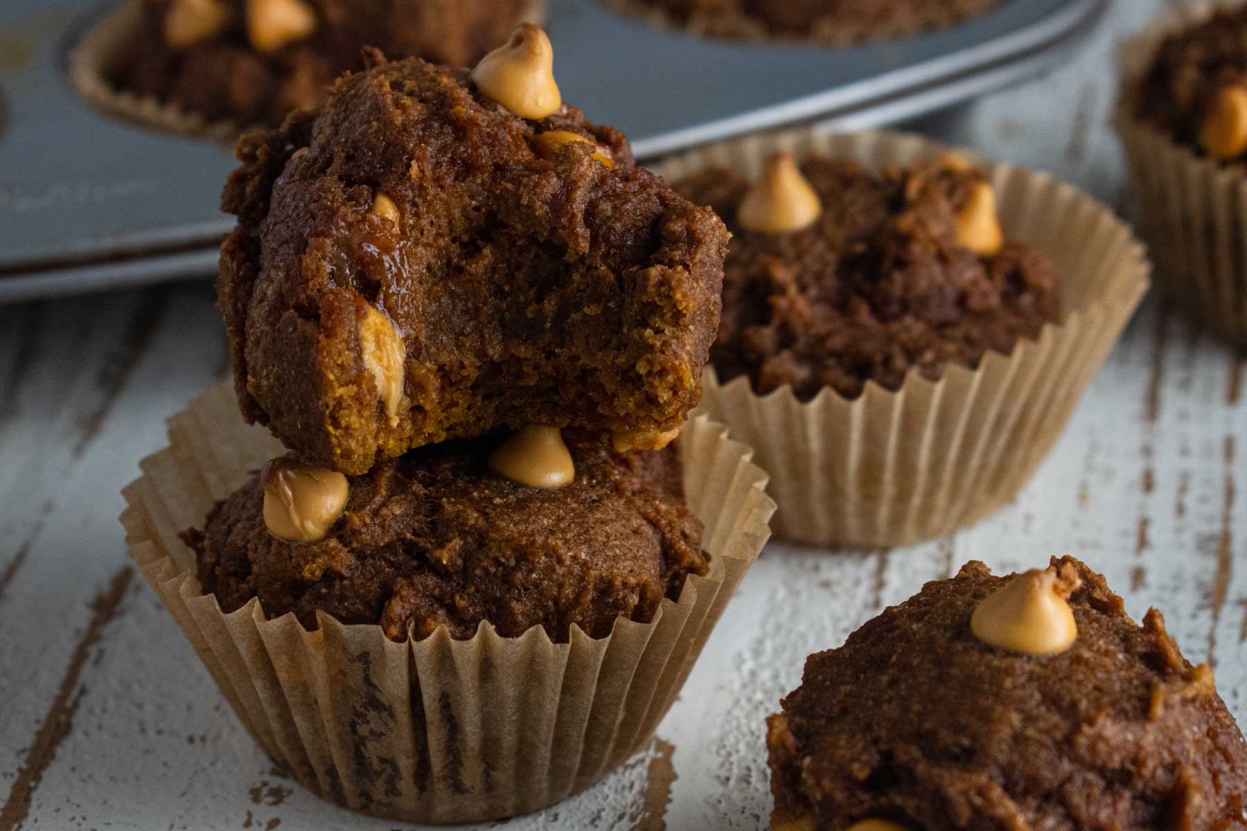 A close up of the pumpkin muffins on a white board with a bite taken out of one of the muffins.