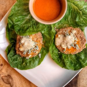 buffalo turkey burgers on romaine lettuce wraps with blue cheese crumbles on top and a container of buffalo sauce