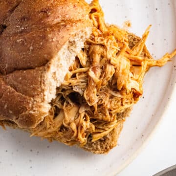 Shredded BBQ chicken in a whole wheat bun on a white plate.