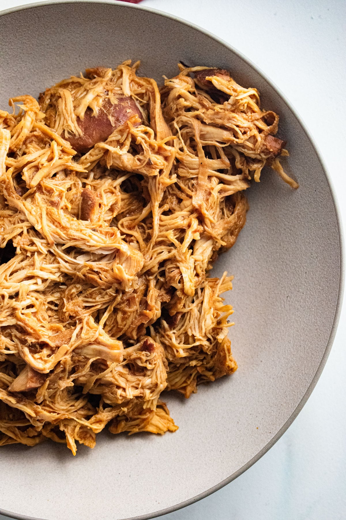 Shredded BBQ chicken in a white bowl on a white table.