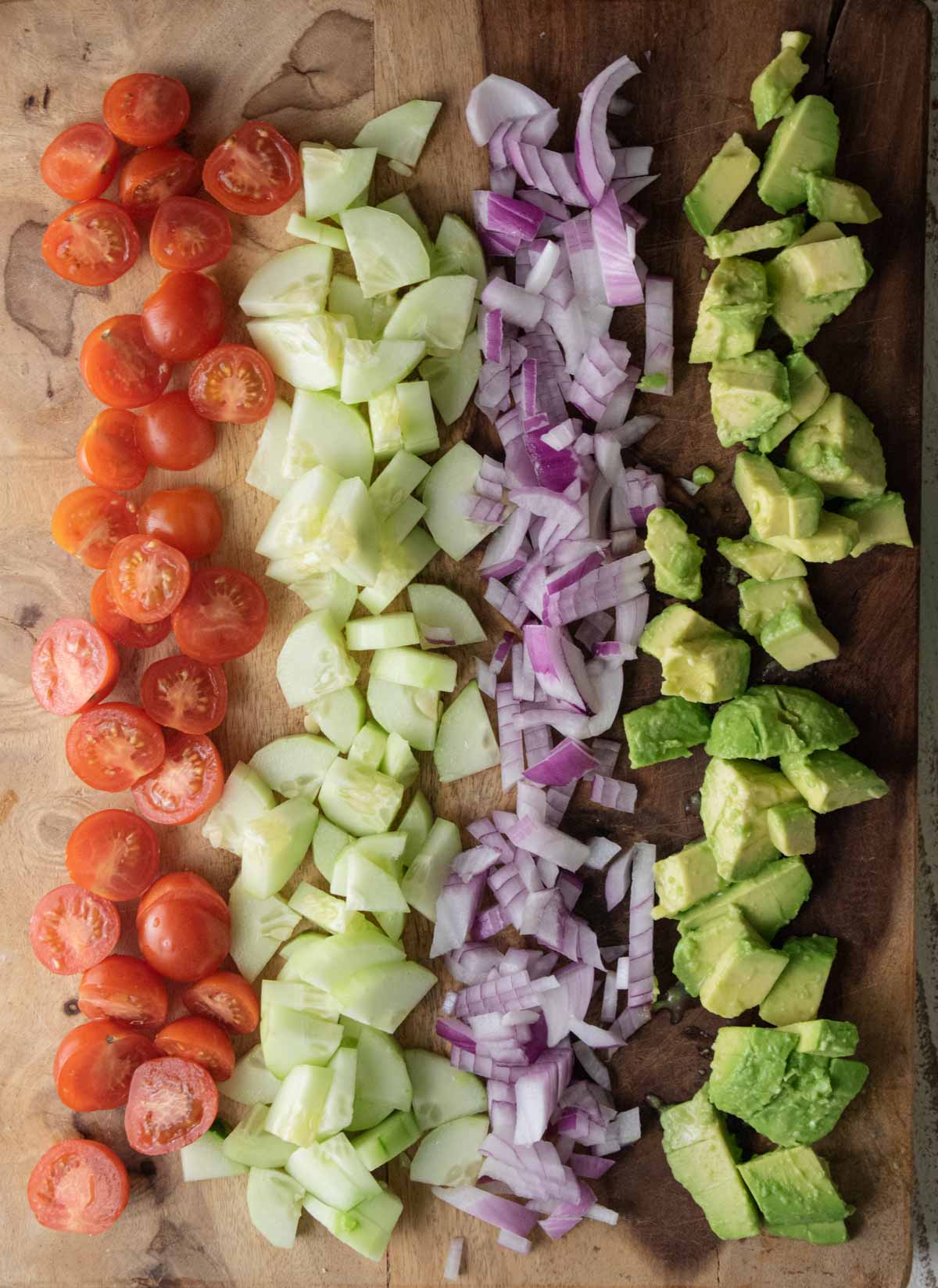 sliced cherry tomatoes, cucumbers, red onions,and avocados on a wooden cutting board