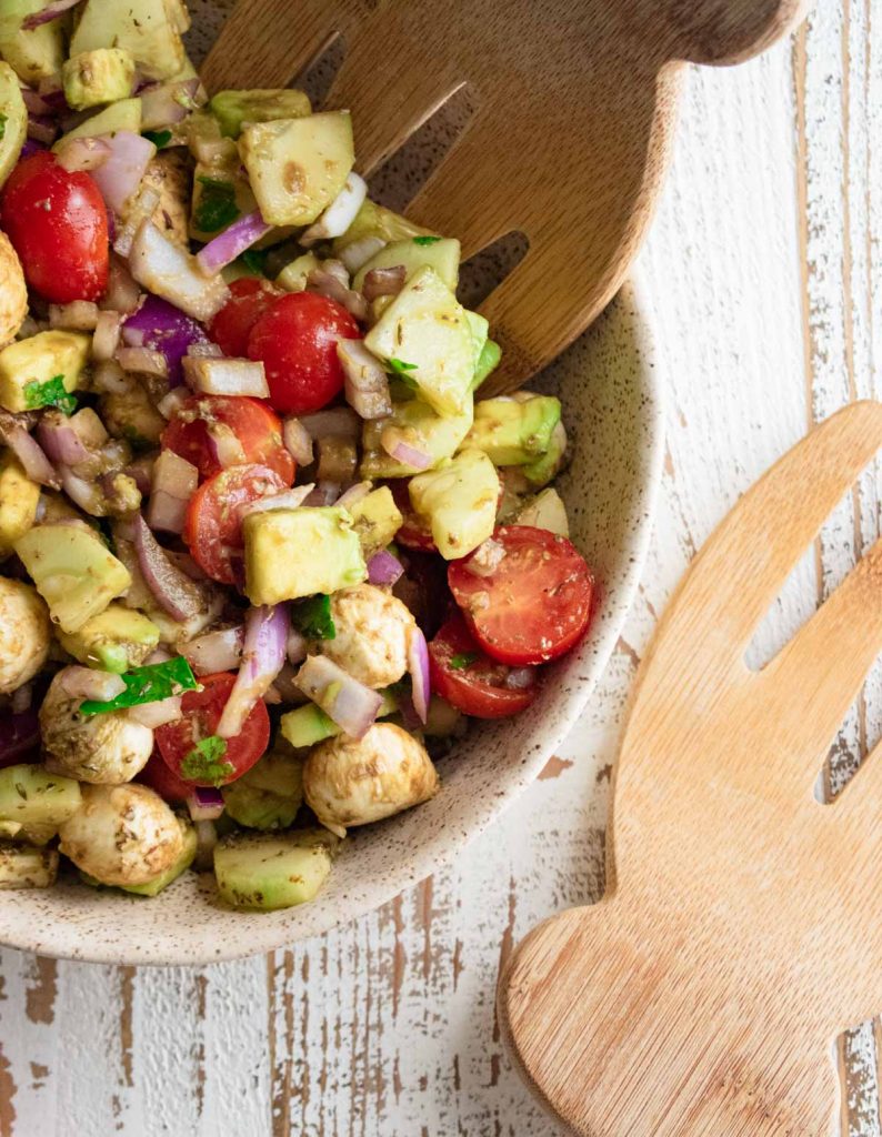 a close up of a fresh juicy summer salad in a tan-colored bowl on a wooden table with a wooden serving fork