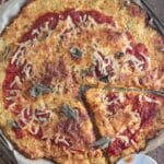 Cauliflower pizza on a piece of parchment paper on top of a wooden table with a pizza cutter laid next to it.