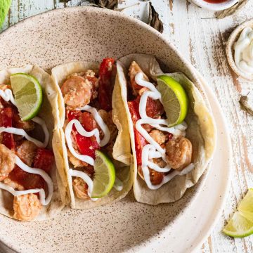 birds-eye view of Mexican shrimp tacos in a white bowl inside corn tortillas topped with red bell peppers and lime slices and drizzled with plain greek yogurt