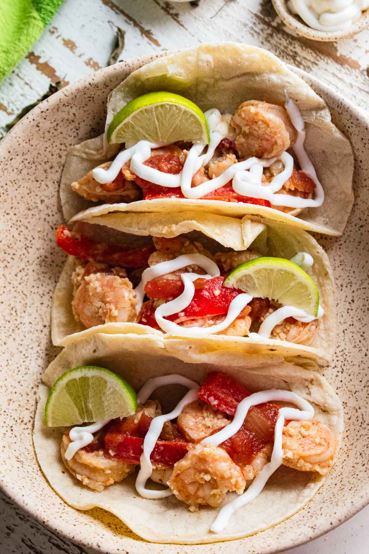 close up of Mexican shrimp tacos in corn tortillas topped with red bell peppers, lime, and drizzled with plain greek yogurt