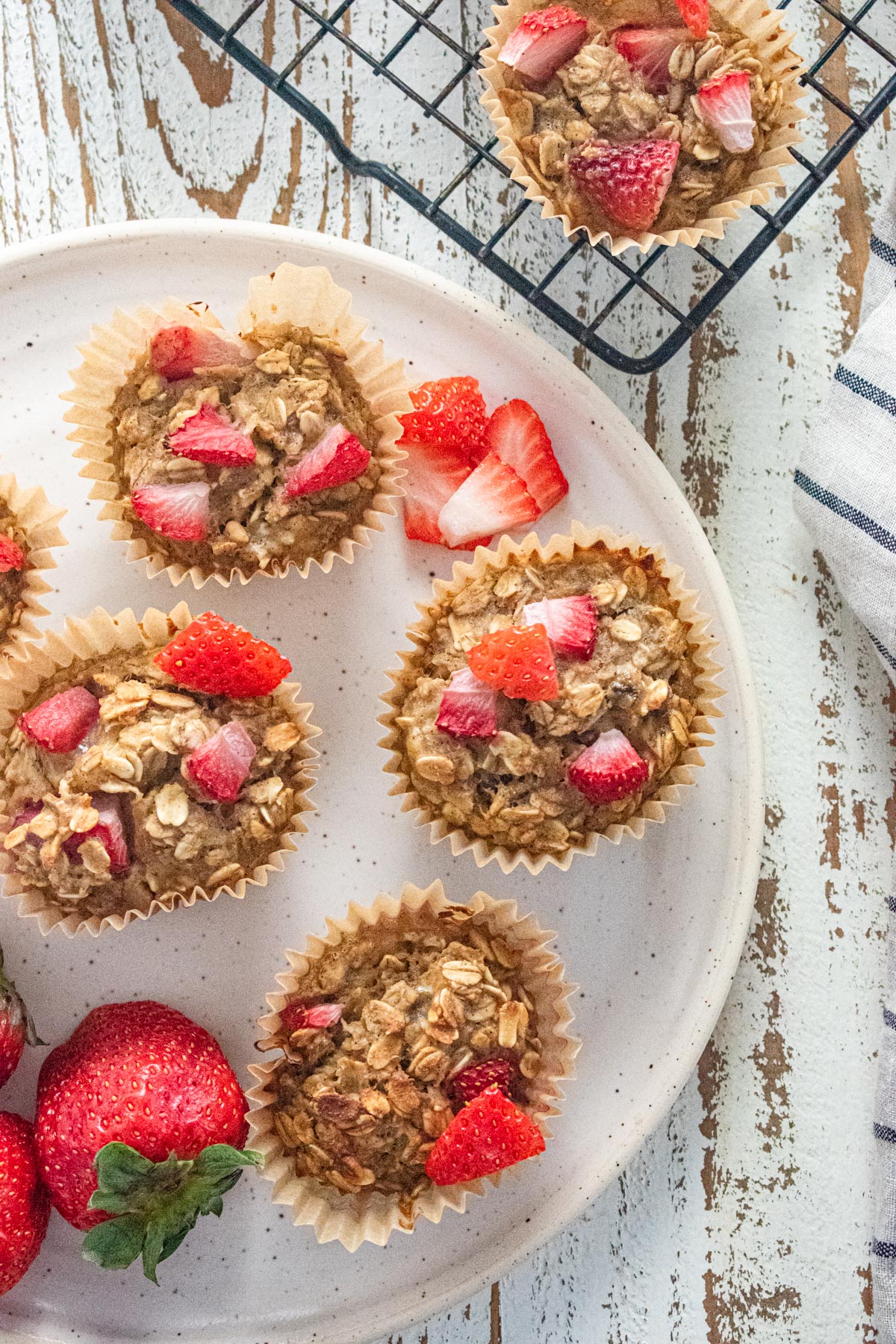 Peanut butter and jelly oatmeal breakfast cups on a white plate and on a cooling rack.