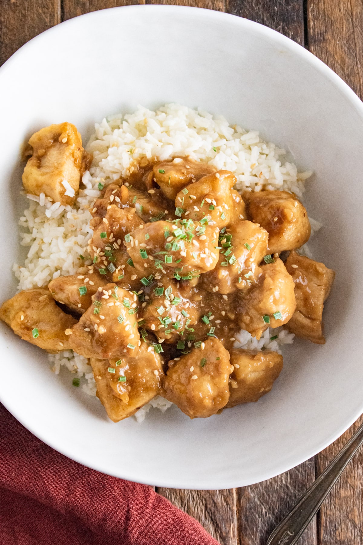 A close up of peanut butter chicken and white rice in a white bowl on a wooden table.