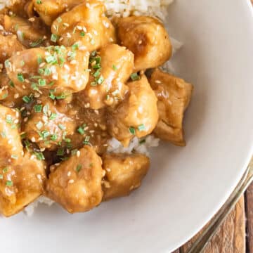 Peanut butter chicken in a white bowl with white rice and topped with herbs.