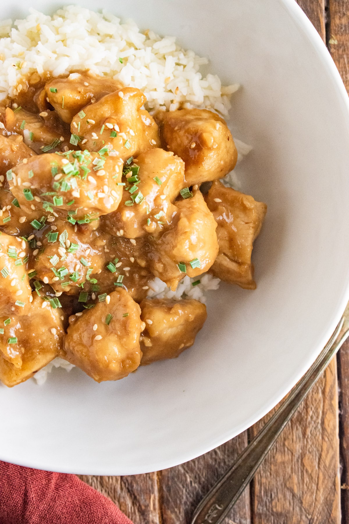 Peanut butter chicken in a white bowl with white rice and topped with herbs.