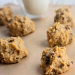 A close up of cookie dough bites on a piece of parchment paper with a glass of milk in the background.