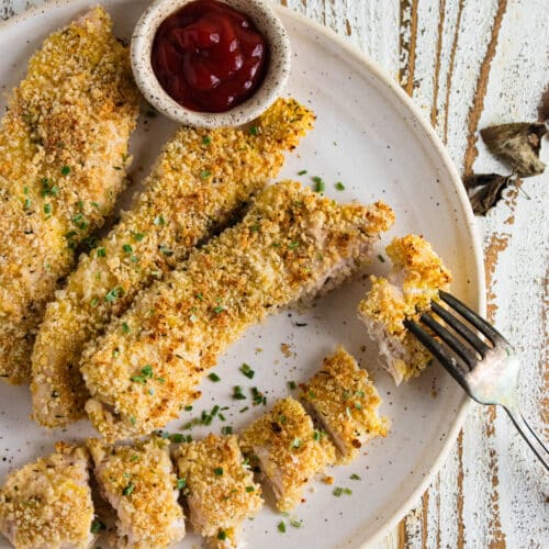 A birds-eye view of crispy panko chicken on a white plate with a ramekin filled with ketchup.