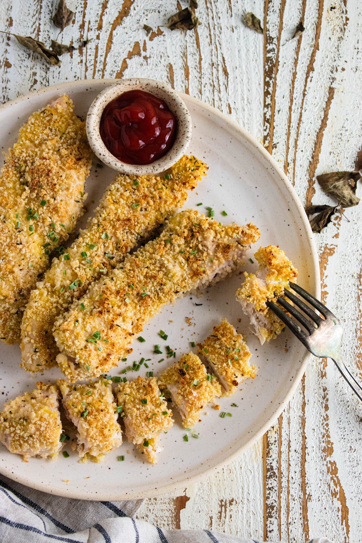 A birds-eye view of crispy panko chicken on a white plate with a ramekin filled with ketchup.