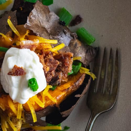 A close up of a fully loaded sweet potato topped with cheese, scallions, bacon, and plain Greek yogurt.