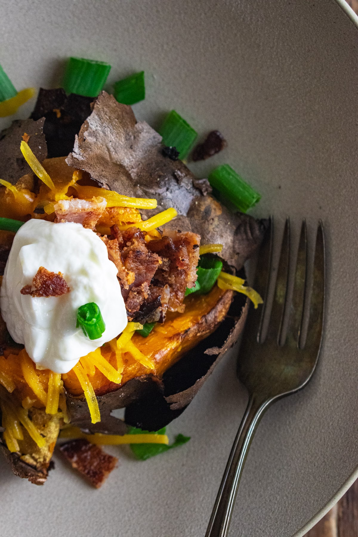 A close up of a fully loaded sweet potato topped with cheese, scallions, bacon, and plain Greek yogurt.