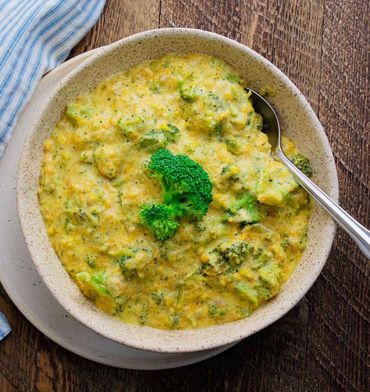 birds eye view of homemade broccoli cheddar soup in a white bowl with a blue and white stripped napkin and a spoon sticking out