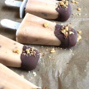 chocolate covered banana peanut butter popsicles topped with walnuts on lined parchment paper