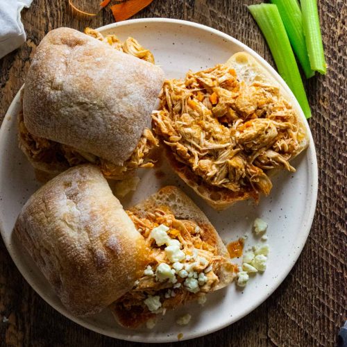 birds eye view of crockpot buffalo chicken siders on a plate with celery sticks and some crumbled blue cheese