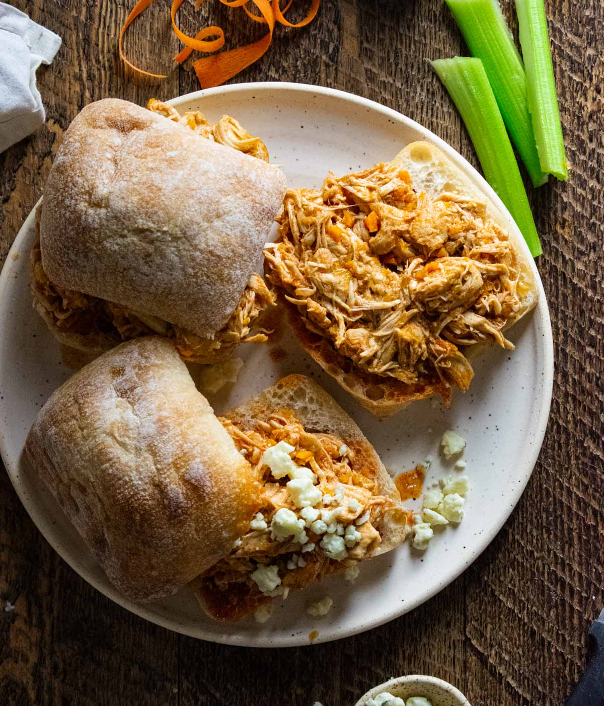 birds eye view of crockpot buffalo chicken siders on a plate with celery sticks and some crumbled blue cheese