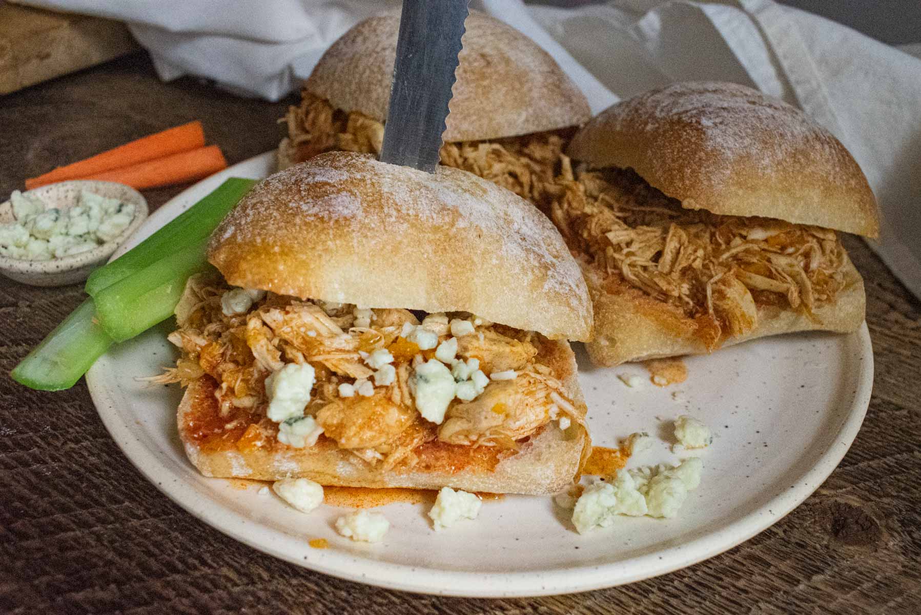 close up of crockpot buffalo chicken on a whole wheat bun with a knife going through it