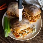 crockpot buffalo chicken sliders on a plate with celery sticks and a knife through the top of the slider