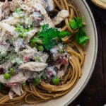 Close up of slow cooker creamy chicken carbonara in a cream colored bowl on a wooden board.