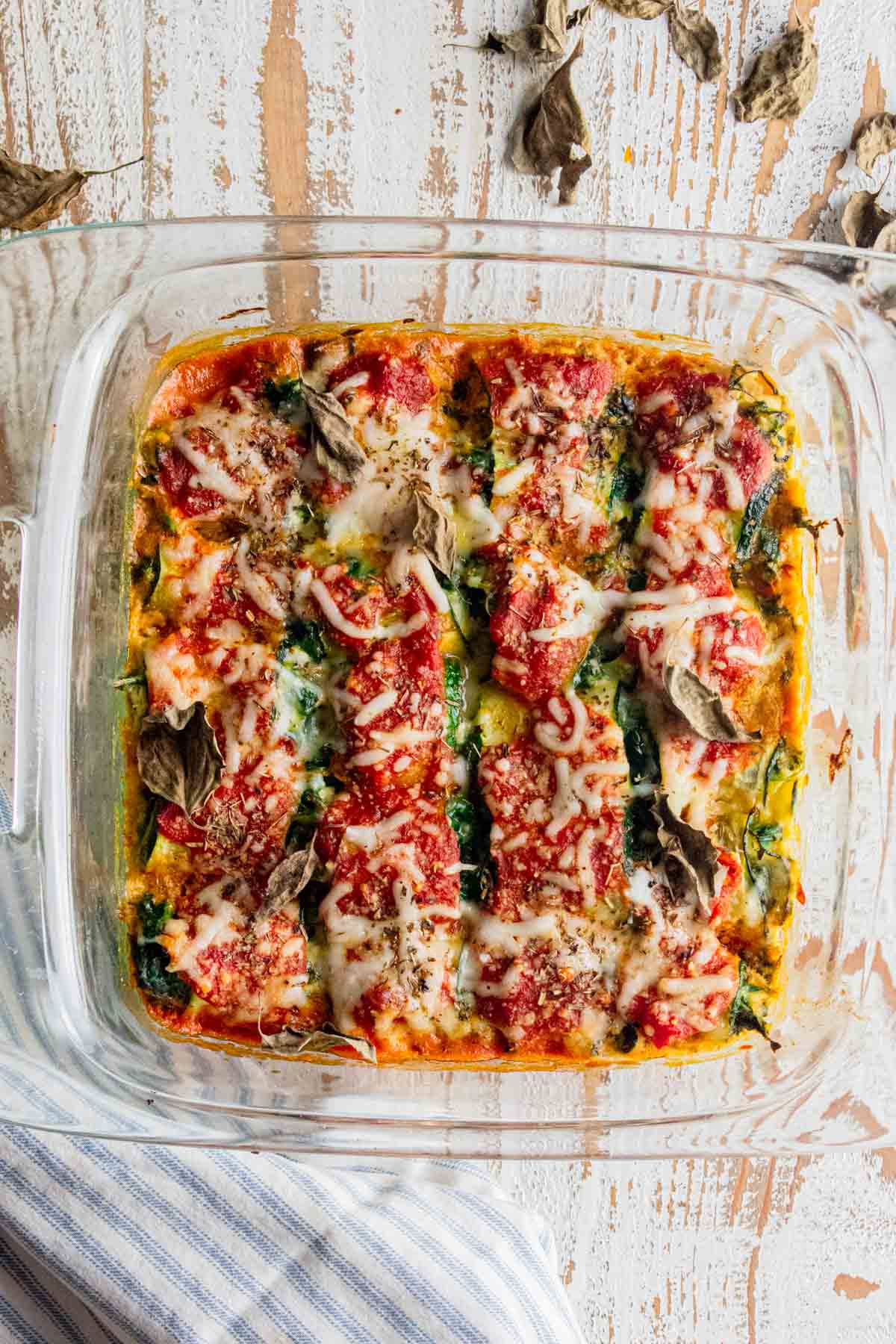 top view of a square glass baking dish with zucchini roll ups inside and topped with marinara sauce and shredded mozzarella cheese