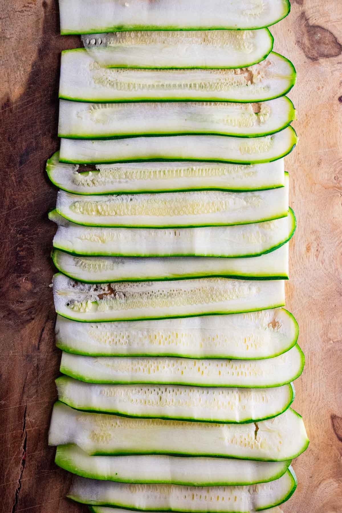 thinly sliced zucchini strips on a wooden cutting board