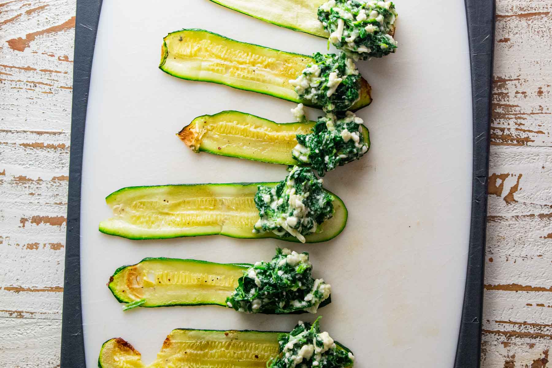 zucchini strips laid on a cutting board with the cottage cheese and spinach filling at the bottom ready to be rolled up