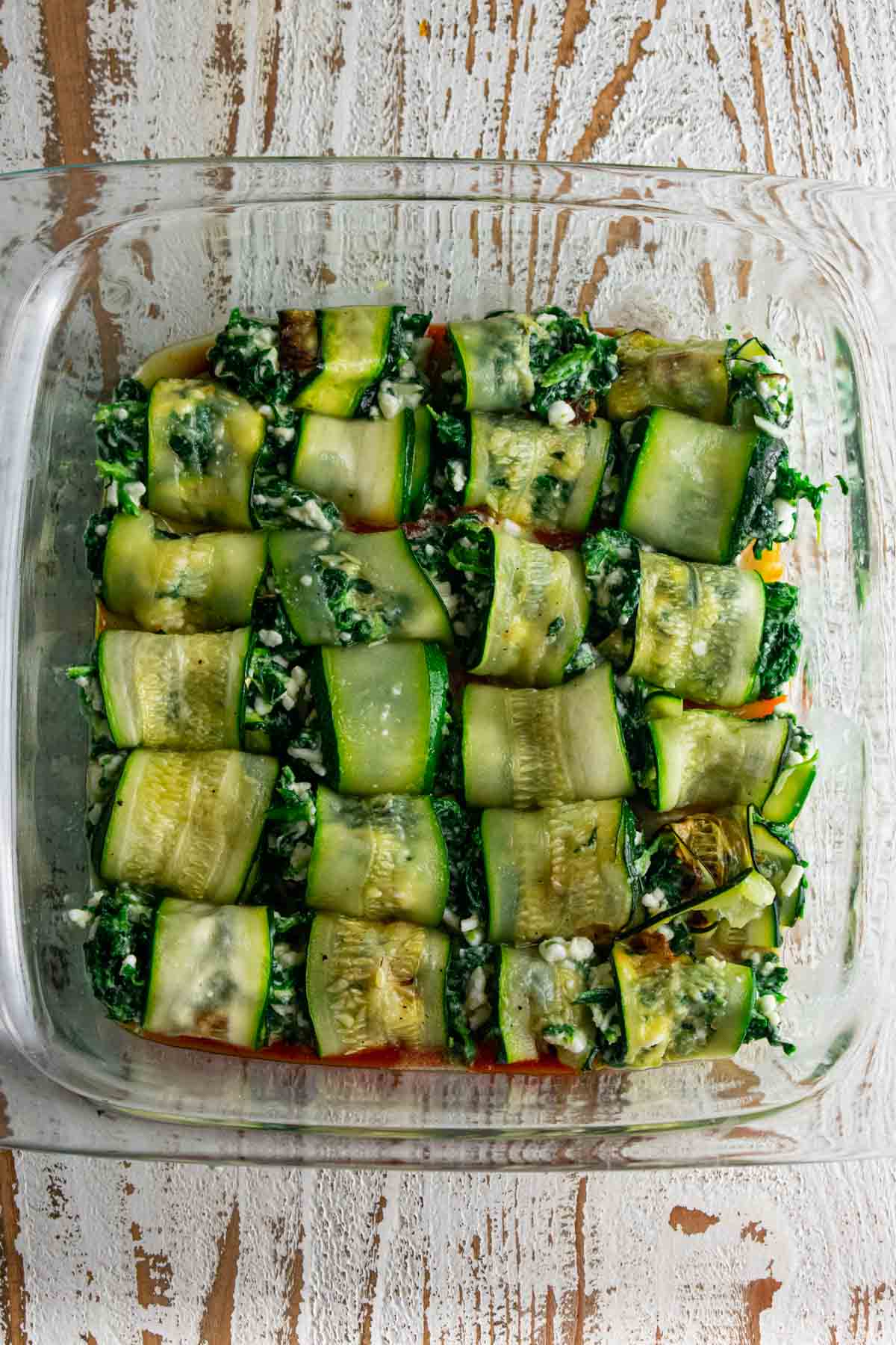 zucchini roll ups placed on top of a marinara filled baking dish