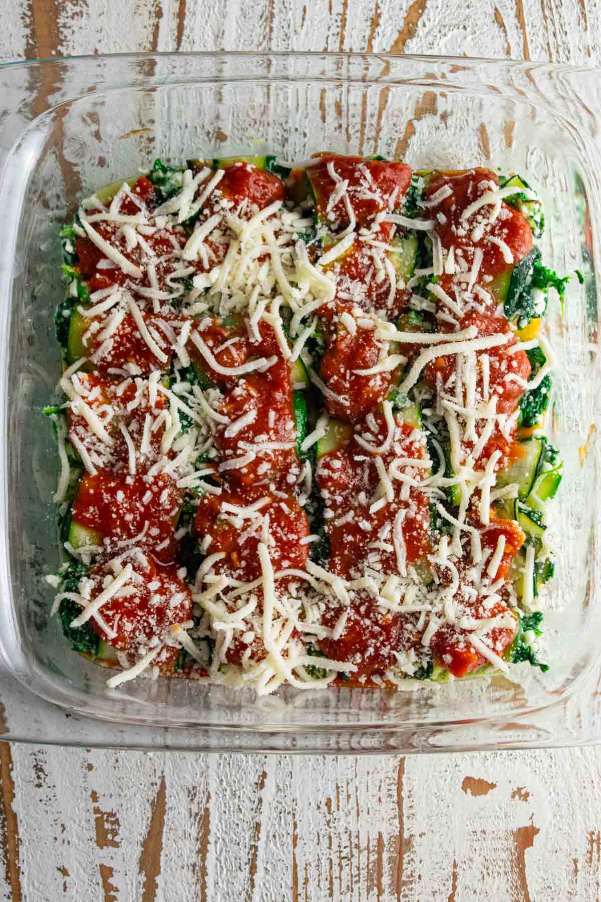 zucchini roll up in a glass baking dish covered with marinara sauce and mozzarella and parmesan cheese