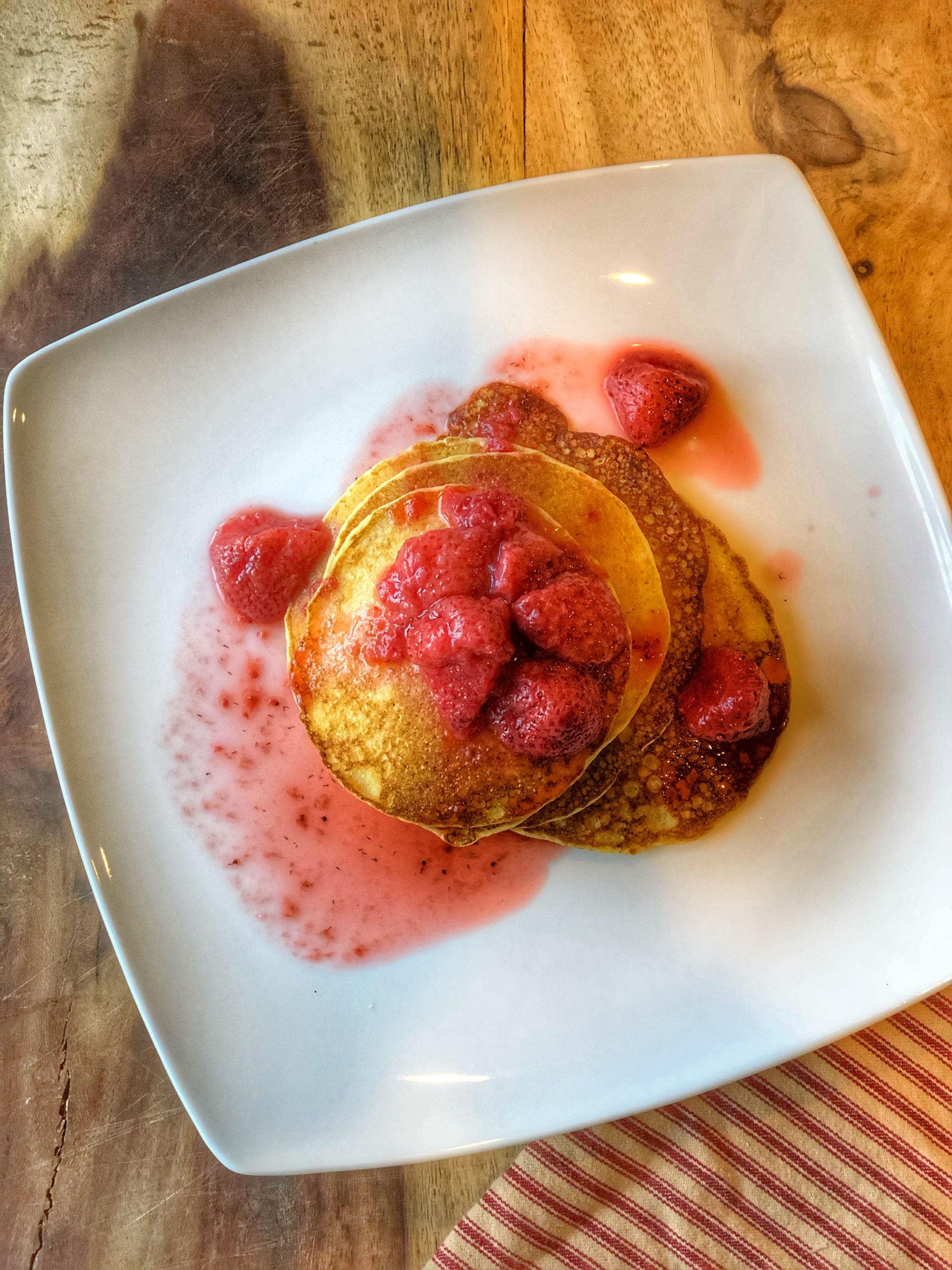 lacy cornmeal pancakes with strawberry compote on a white plate on a wooden board