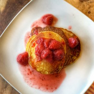 strawberry compote over cornmeal pancakes on a white plate on a wooden board