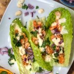 shrimp tacos in romaine lettuce leaves topped with red onion and cilantro on a white plate