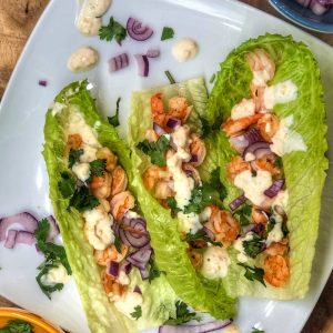 shrimp tacos in romaine lettuce leaves topped with red onion and cilantro on a white plate