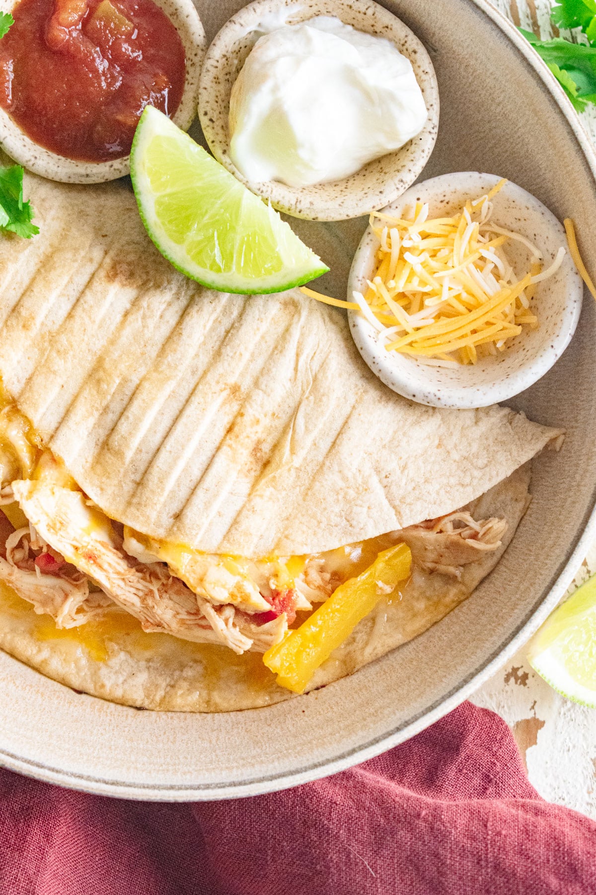 A close up of chicken fajitas on a cream colored plate with salsa, plain Greek yogurt, and cheese and a lime slice.