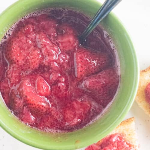 A close up of strawberry compote in a green bowl with a slotted spoon.