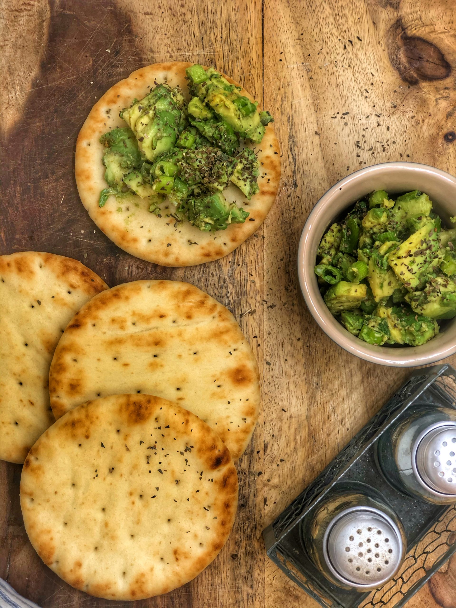 avocado and scallion salsa in a small bowl on a wooden cutting board with mini naan breads