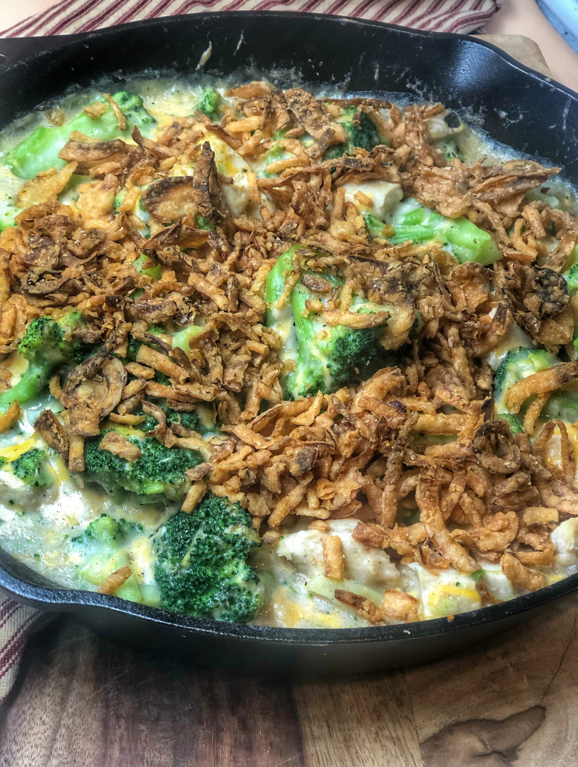 close up of chicken and broccoli casserole in a cast iron skillet on a wooden cutting board