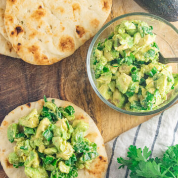 Avocado scallion salsa on mini naan bread on a wooden cutting board.