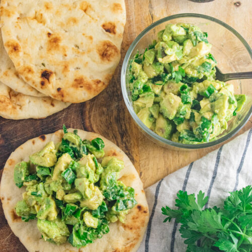 Two mini flatbreads topped with avocado and scallion salsa on a wooden cutting board.