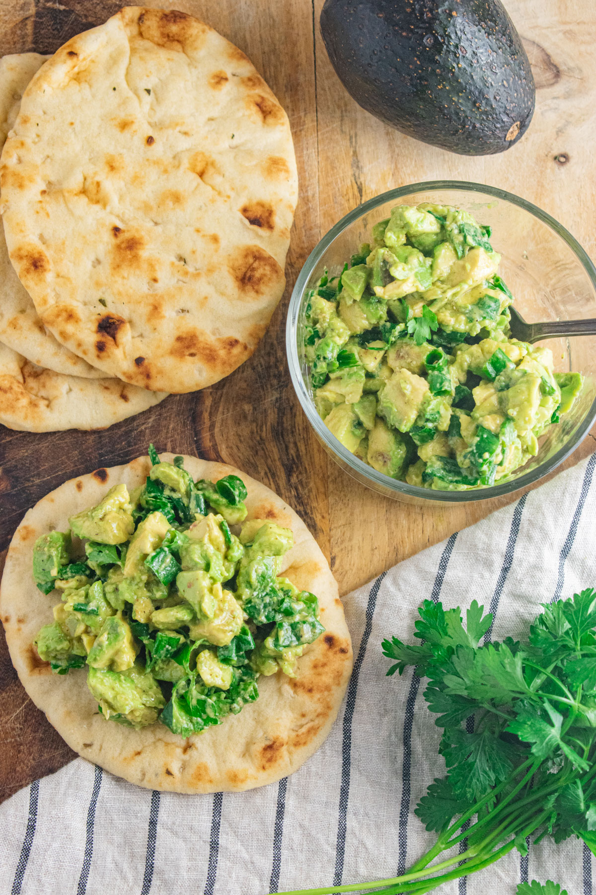 Two mini flatbreads topped with avocado and scallion salsa on a wooden cutting board.
