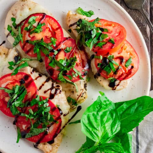 Chicken Caprese on a white plate topped with drizzled balsamic vinegar and fresh basil leaves.