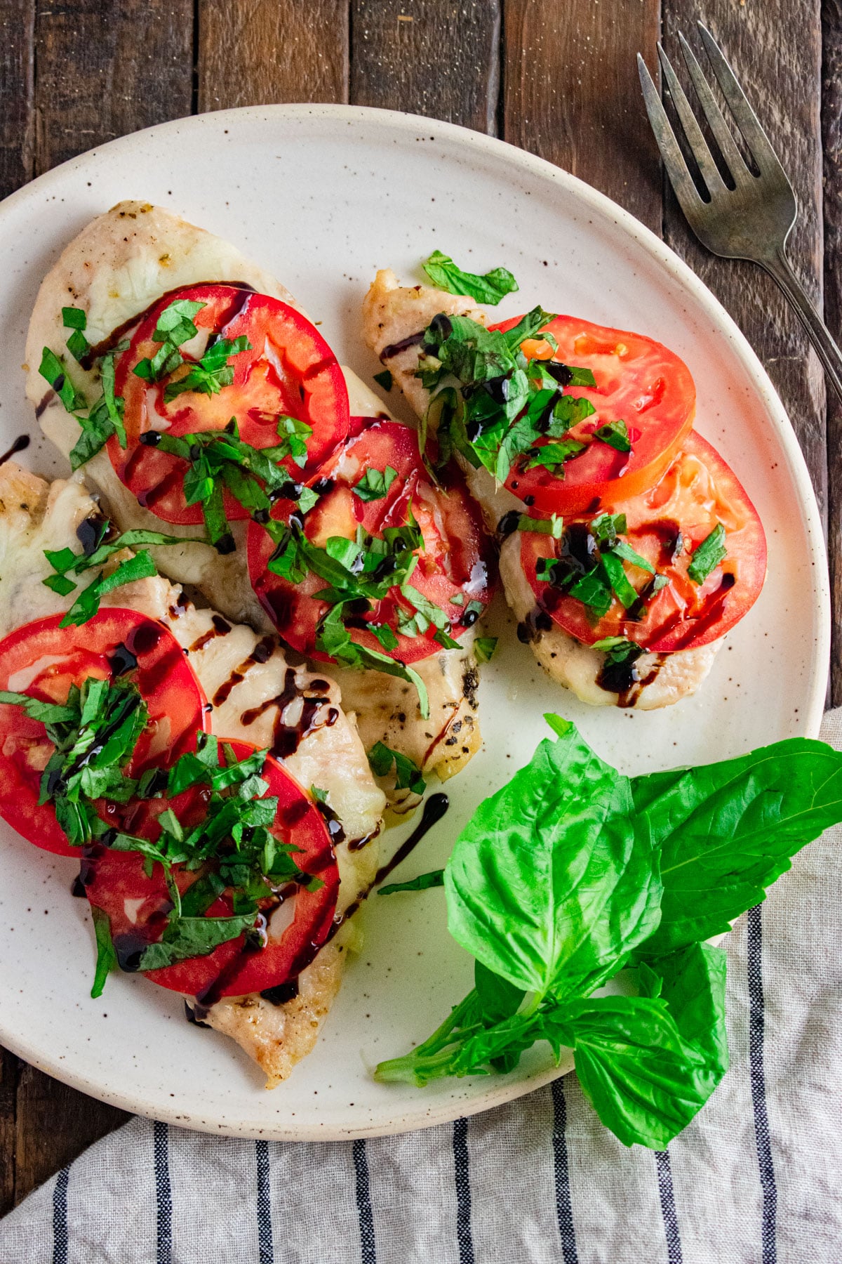 Chicken Caprese on a white plate topped with drizzled balsamic vinegar and fresh basil leaves.