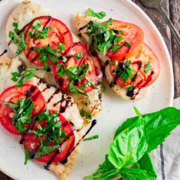 Birds-eye view of baked chicken caprese on a white plate with balsamic glaze drizzled on top with fresh basil on top.