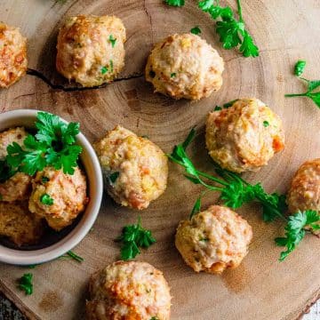 Top view of Italian chicken meatballs on a wooden board with fresh parsley scattered around.