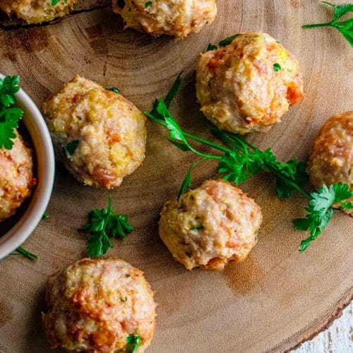 close up of italian chicken meatballs on a wooden tray with scattered fresh parsley