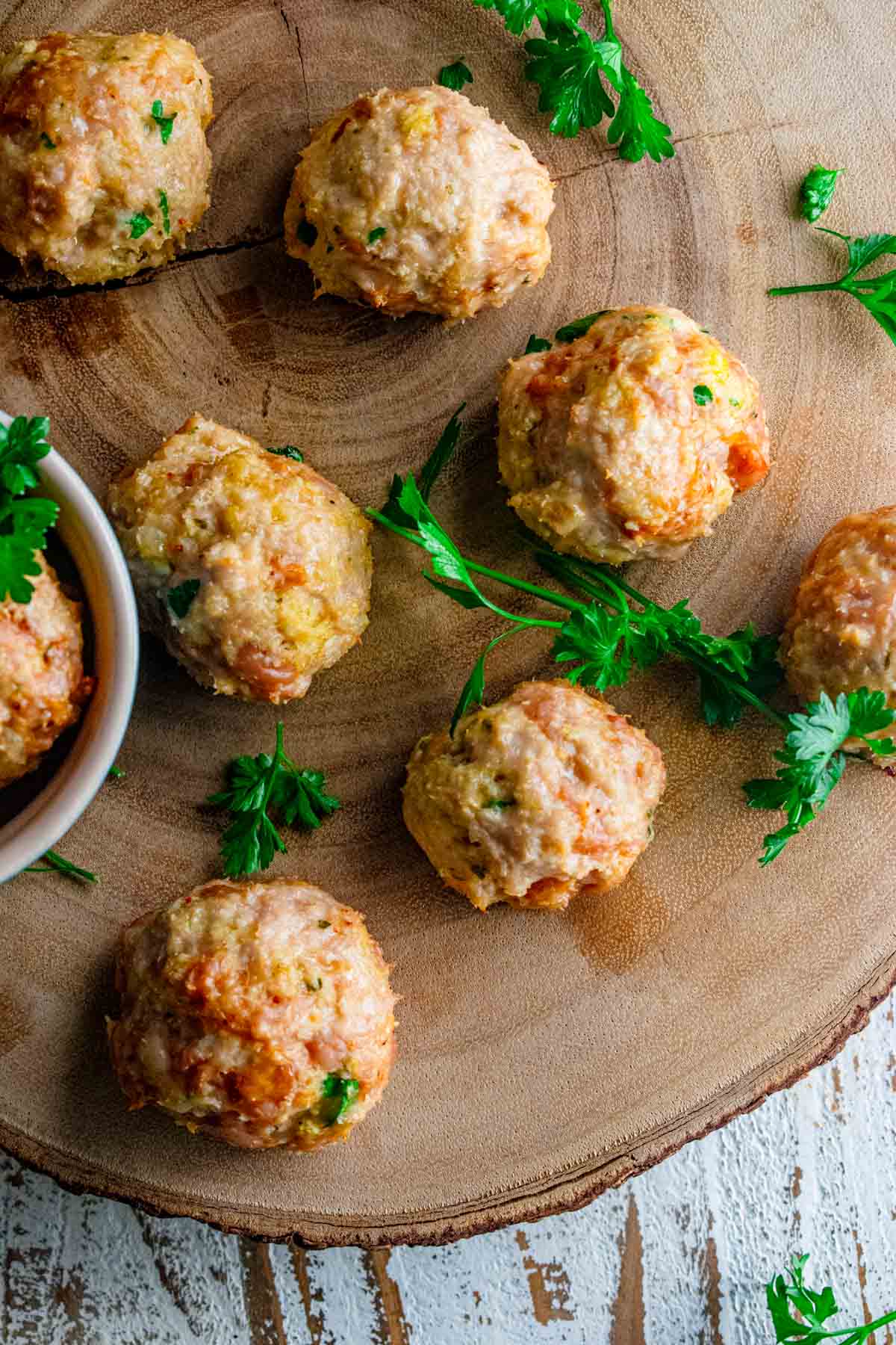 close up of italian chicken meatballs on a wooden tray with scattered fresh parsley