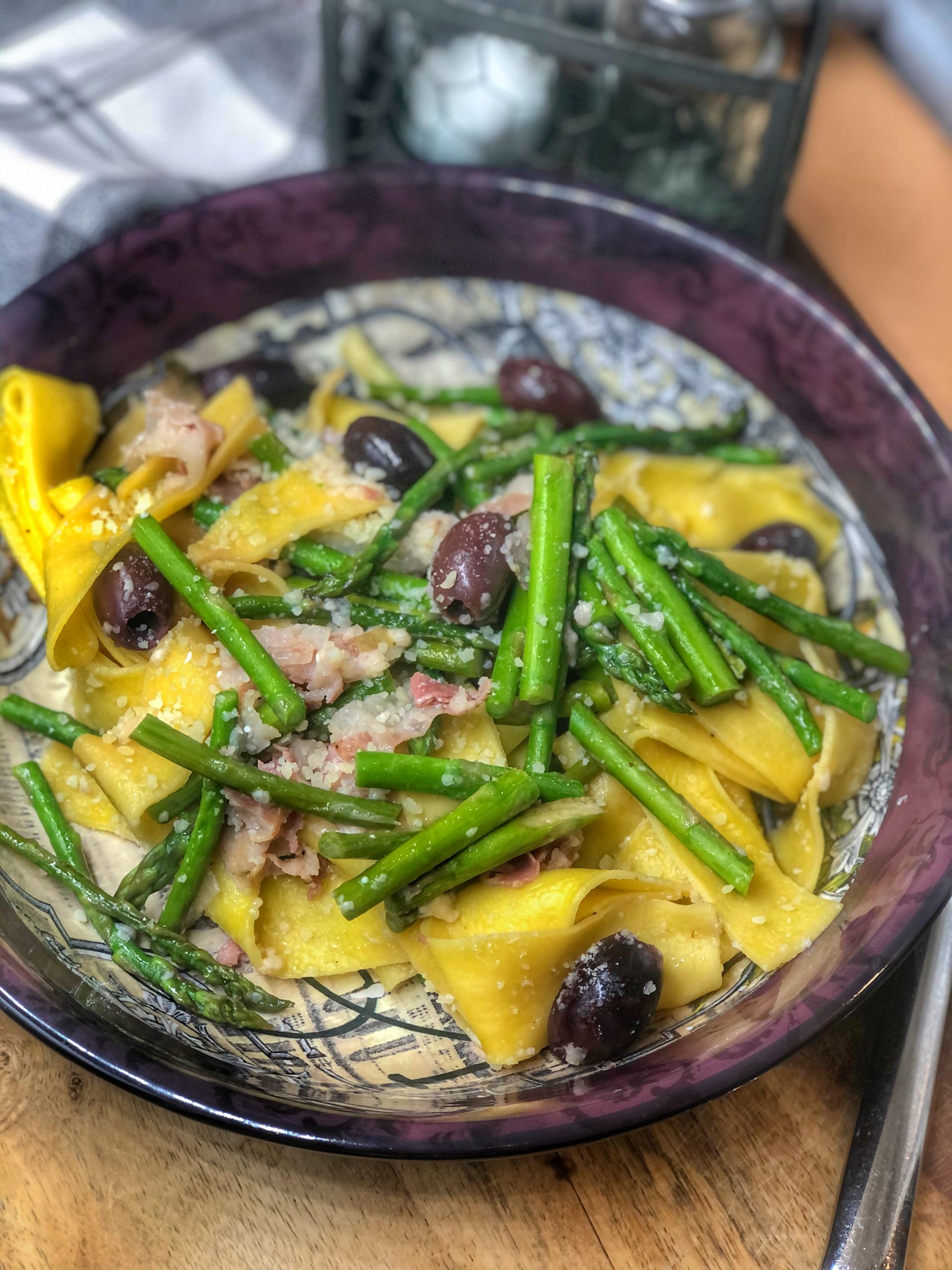 asparagus olives and pancetta paparadelle in a maroon bowl on a wooden board