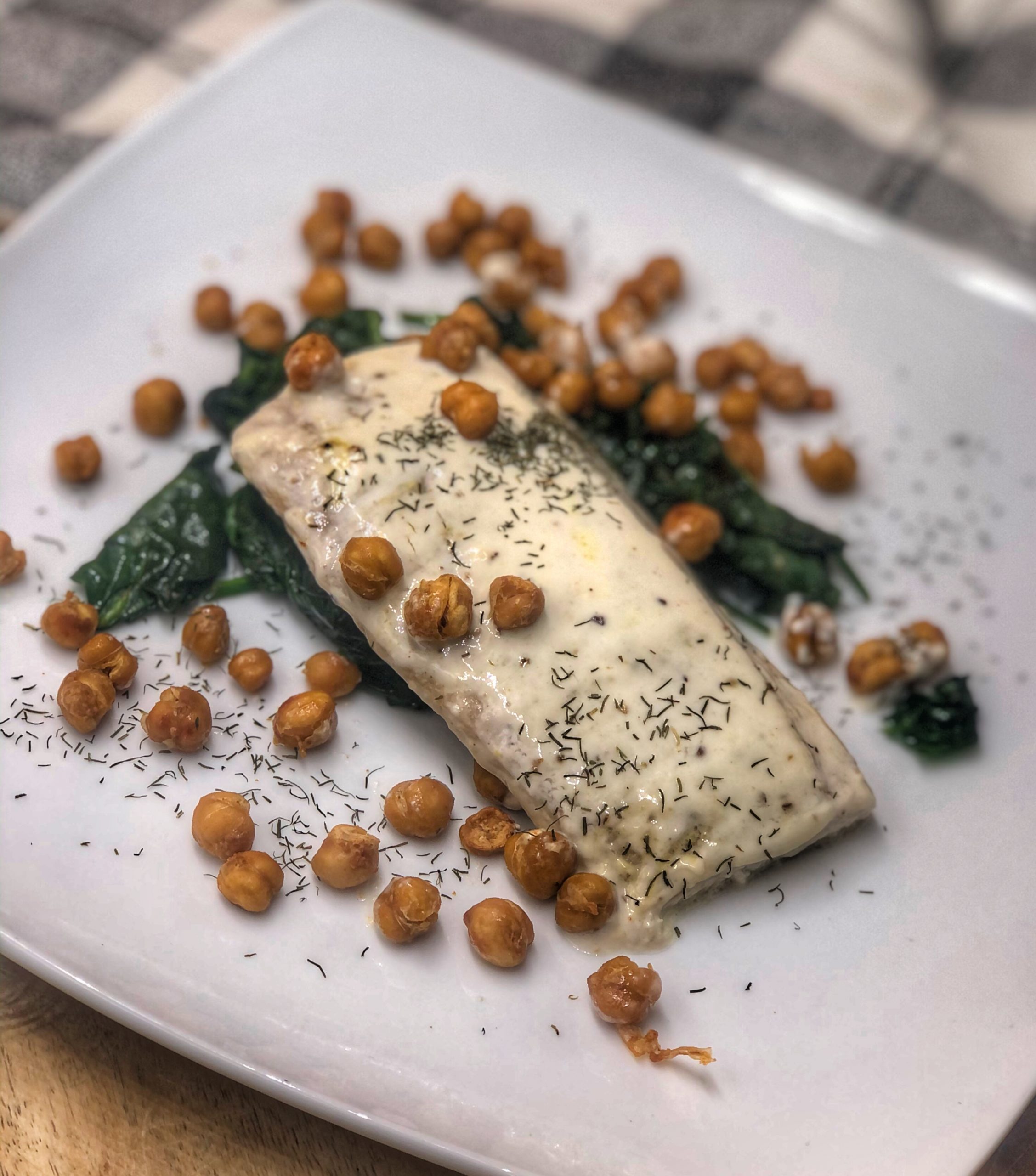 roasted mahi mahi and chickpeas over spinach on a white plate on a wooden board